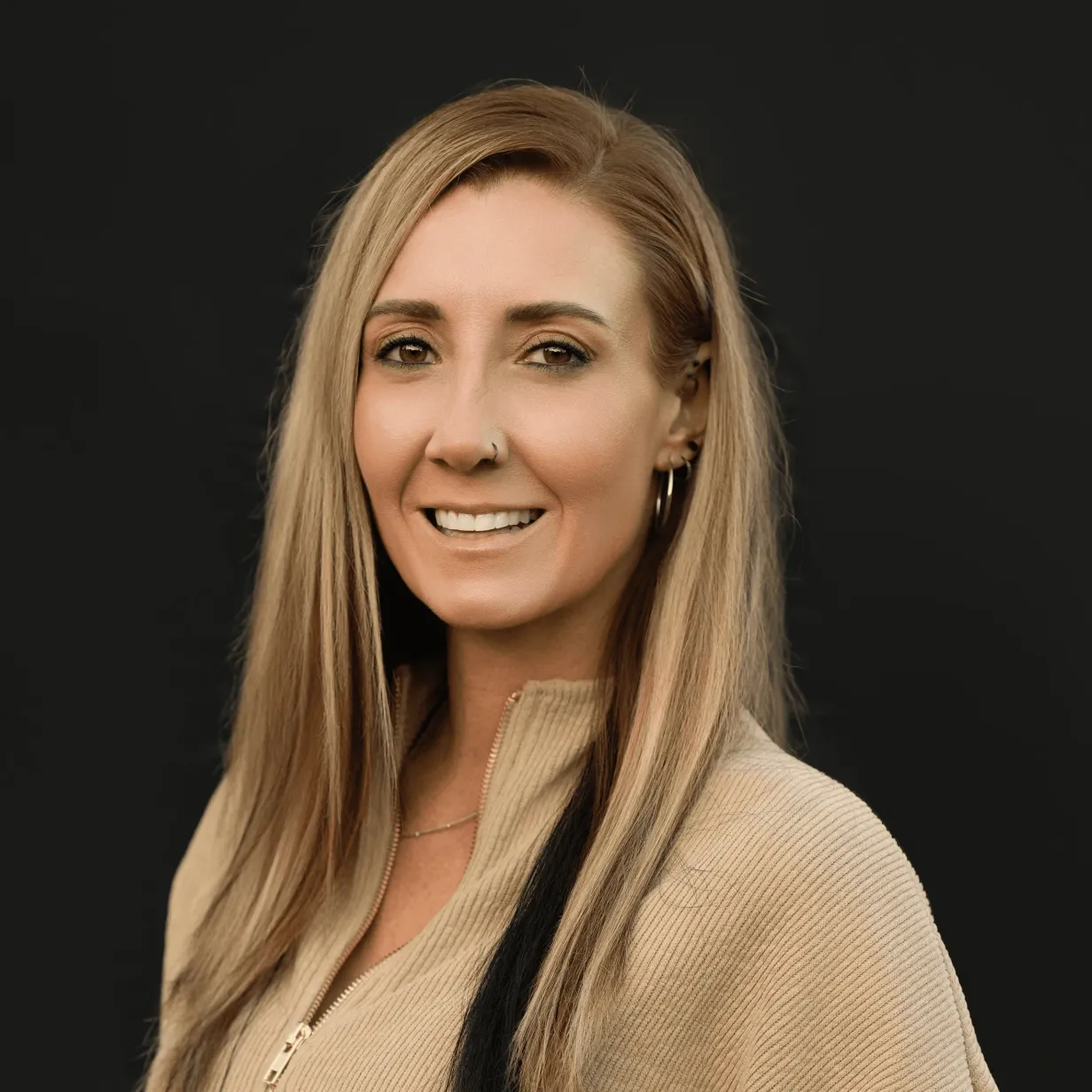 Portrait of Amy Musty, founder of ABC Au Pair, smiling in a beige sweater against a dark background