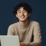 Smiling young man with curly hair sitting at a laptop