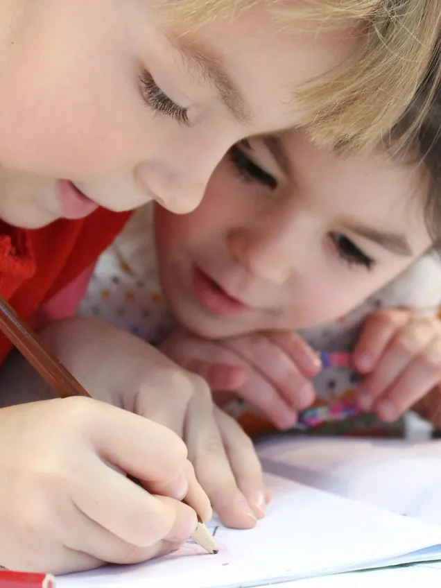 Two children writing in a notebook with coloured pencils