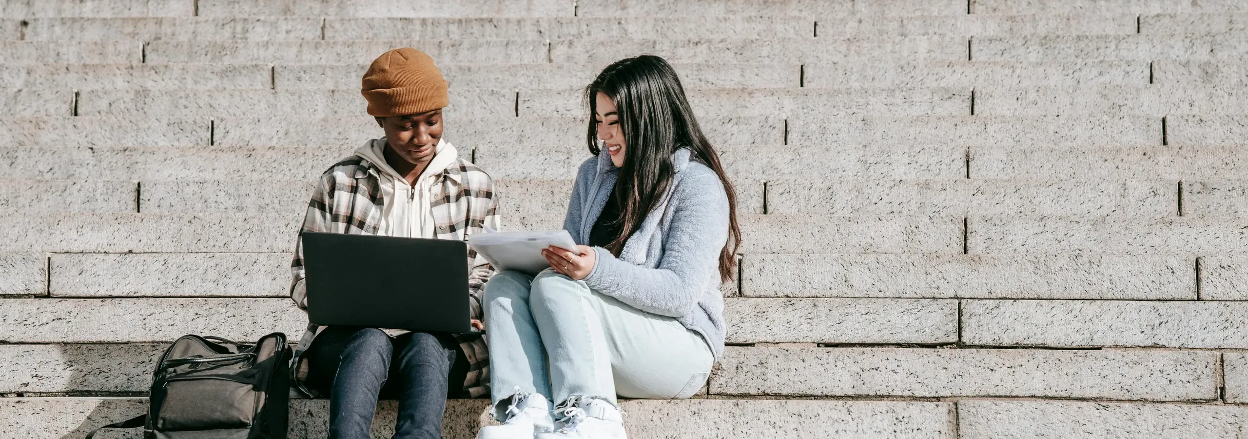 Two students sitting on wide stone steps, looking at a laptop together